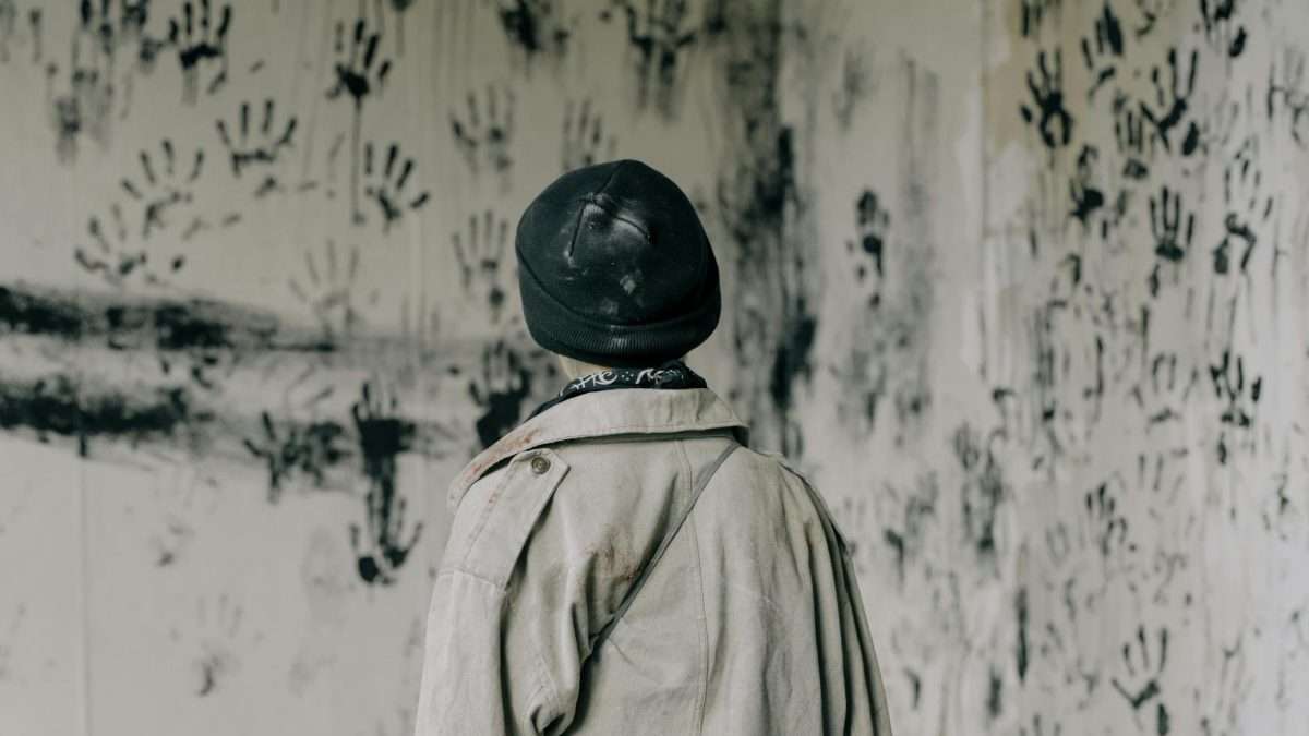 person in brown coat and black hat standing near white and black floral wall