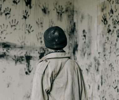 person in brown coat and black hat standing near white and black floral wall